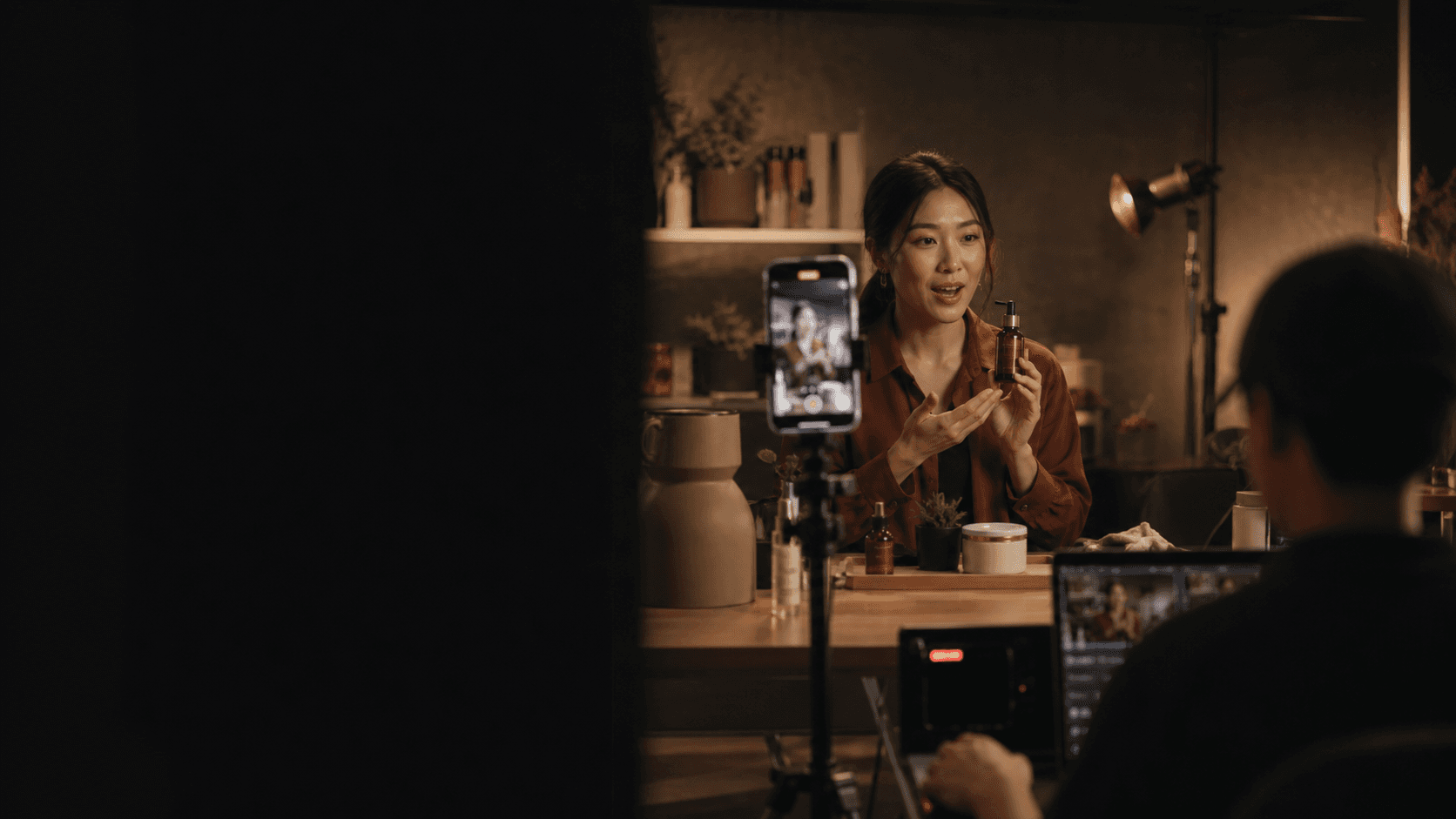 A livestream host presenting a product to a phone camera in a warm studio